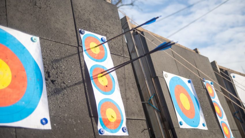 A detailed shot of arrows piercing through colorful archery targets on an outdoor range.