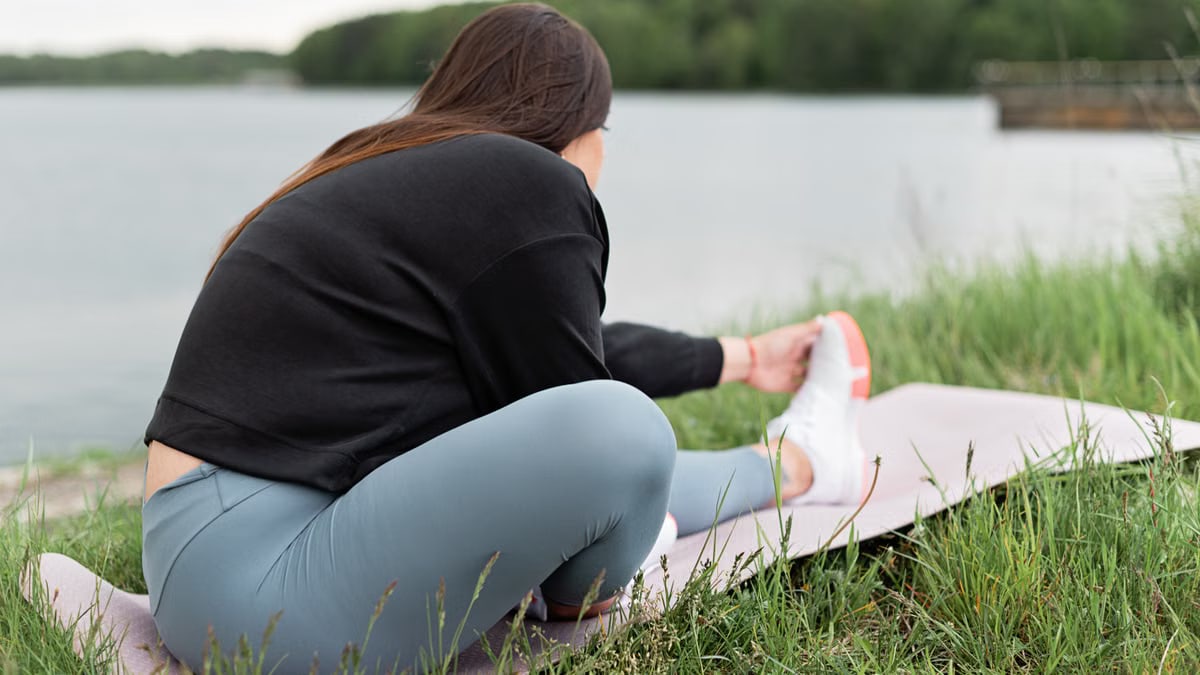 Woman doing stretching exercises on a yoga mat outdoors by a serene lake.